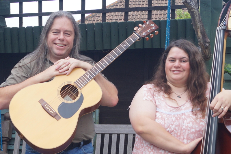 Photograph of David Rozzell wearing a OOO-18 acoustic guitar, stood next to Clare Rozzell leaning on a double bass.